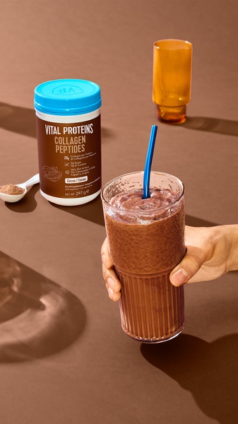 A high-quality 9:16 vertical image featuring a jar of collagen powder next to a prepared chocolate protein shake, styled in a warm, minimalist aesthetic.